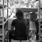 Usine chinoise de fabrication de chaussures. Ouvrier sur chaine de production, de dos, assis sur un minuscule tabouret couche de cote. Chine, Shenzhen, usine du monde. Travail plus de 70 heures par semaine, a faible couts, pour utilisation des produits par les pays "riches". Made in China.
Derriere lui se trouve le reste de la chaine de production avec les ouvriers.