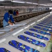 Usine chinoise de fabrication de skateboards. Ouvriers a la chaine, en train de realiser des serigraphies de skate. Chine, Shenzhen, usine du monde. Travail plus de 70 heures par semaine, a faible couts, pour utilisation des produits par les pays "riches". Réalisation des graphismes des planches de skate.