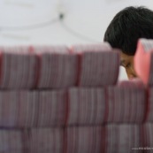 Usine en Chine. Ouvrier derriere sa pile de produits.